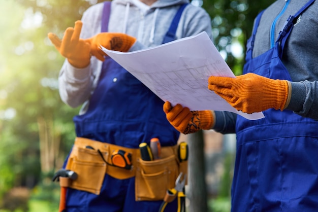 Nuovo progetto. immagine ravvicinata di due costruttori in piedi all'aperto con un progetto aperto che discutono della costruzione del cottage