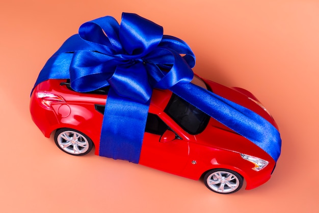 New red car with a blue bow as a gift on coral 