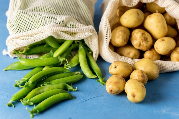 New Ripe Potato and Green Raw Peas in Eco Bags Blue Background Horizontal