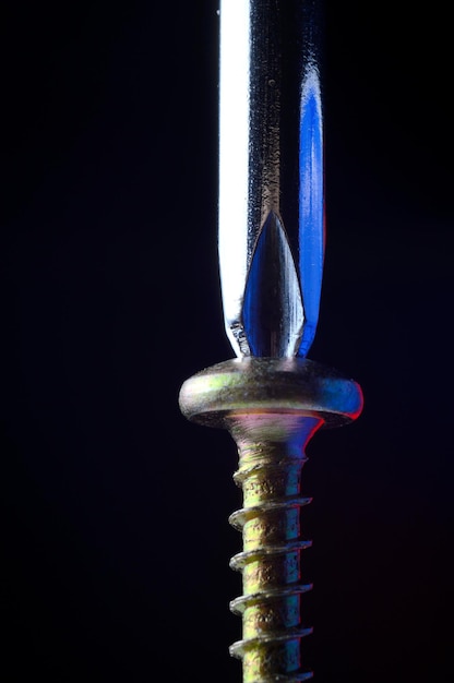 A new selftapping screw and a chrome screwdriver tightens it dark background closeup