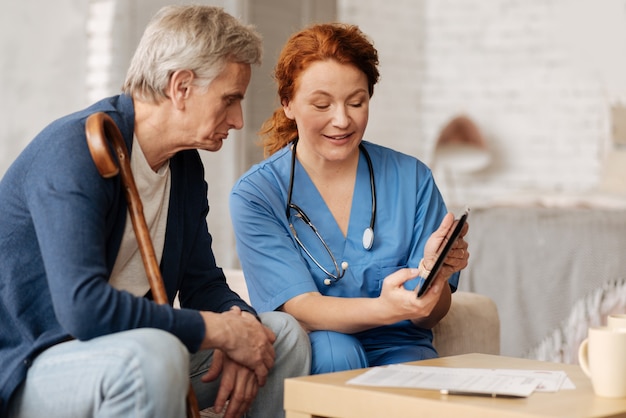 Nuove tecnologie. meraviglioso operatore sanitario positivo che impiega il suo gadget per illustrare il suo discorso sul gentiluomo di farmaci che necessita di guarigione