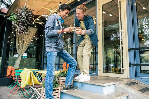 New technology. Joyful delighted friends looking at each other while checking a modern gadget