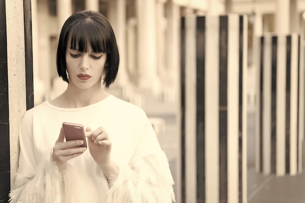 Новые технологии для современной жизни Женщина с красными губами использует смартфон в Париже, Франция Женщина с каштановыми волосами держит мобильный телефон Красивая девушка с сексуальным взглядом Фотомодель с мобильным устройством