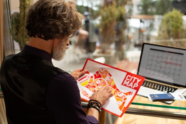 Photo new in town. focused man sitting in the cafe with a city map in his hands pointing on it exploring the map before going for a walk.