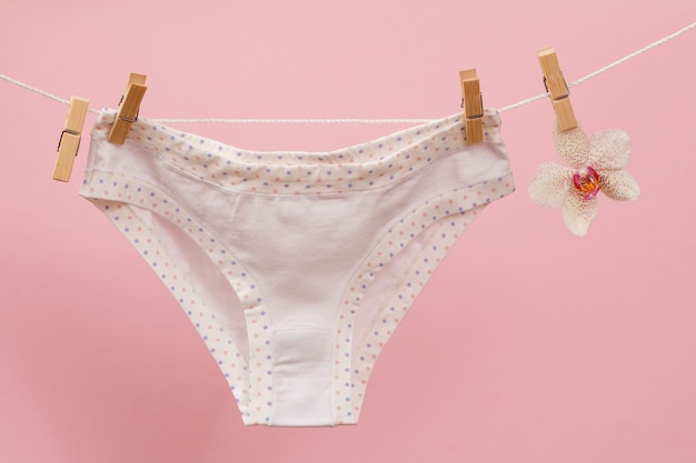 New, white panties on clothesline with clothespins and orchid flower in pink background. Woman underwear.