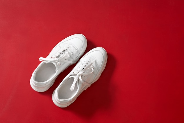 New white trendy sneakers for women on red wall table.