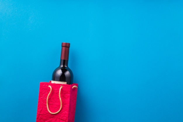 New wine bottle in red paper bag against blue backdrop