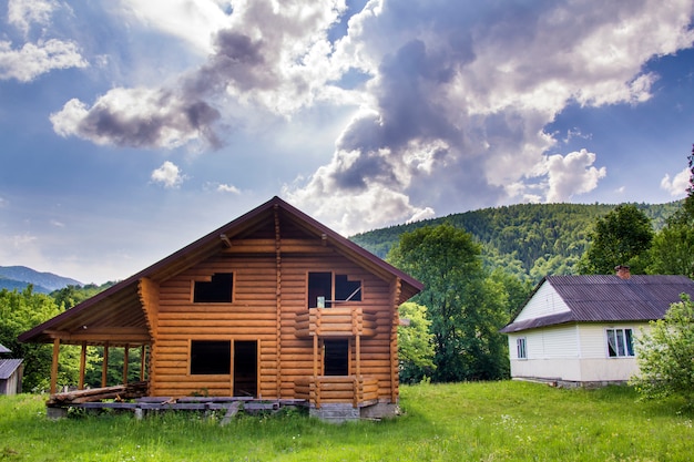 Foto nuovo cottage ecologico in legno con balcone, terrazza, tetto ripido di materiali naturali in costruzione su prato erboso su colline boscose. tradizioni antiche e moderno concetto di costruzione.