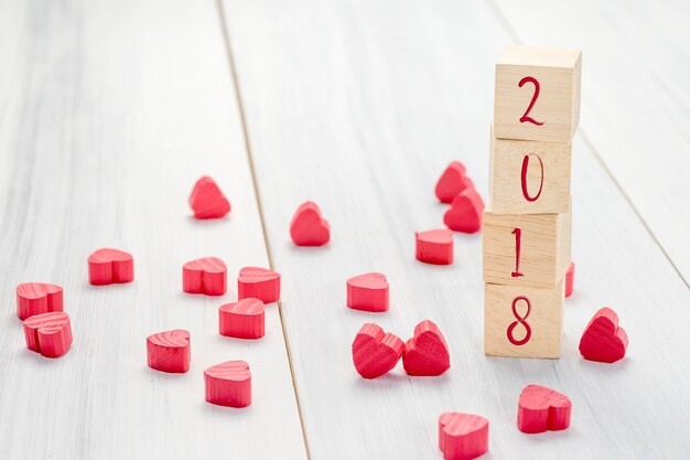 Numero del nuovo anno 2018 sul cubo di legno della pila con il gruppo di mini cuore rosso sulla tavola di legno bianca della plancia