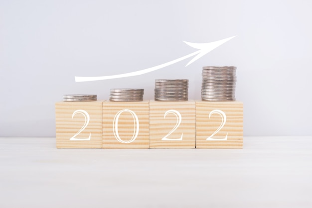 Концепция нового года 2022. Деревянные блоки с текстом 2022 года, монетами и стрелкой вверх. Концепция финансового роста.