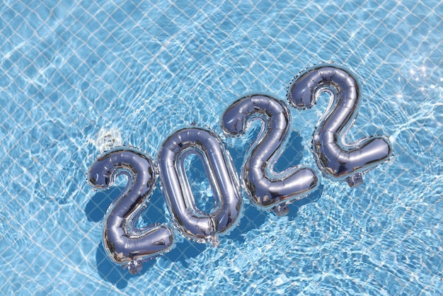 New Year 2022 inflatable figures on blue water in the pool, close-up. Silver numbers balloons, decor. Celebration, holiday