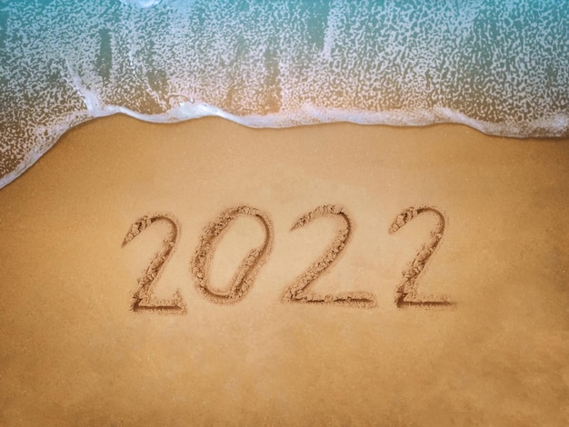 New Year 2022 lettering on the beach with wave and blue sea Numbers 2022 year on the sea shore