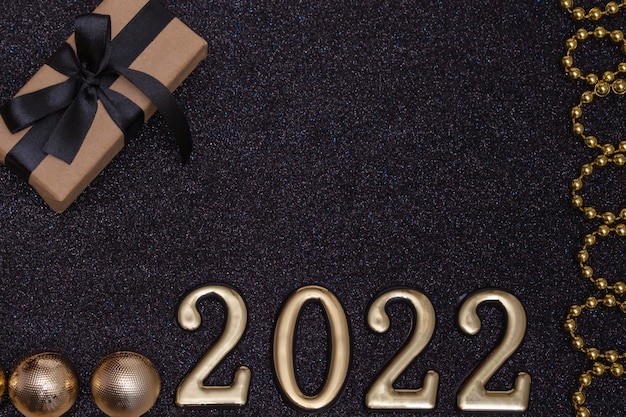 新年2022年。黒い光沢のある背景の上面図新年のモックアップ：赤いリボン、ギフトボックス、金の数字と色とりどりの輝き。はがき、招待状のレイアウト。