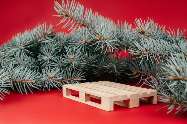 New Year 2022. Wooden pallet on red surface with Christmas tree branches. Podium, pedestal or stage. Merry Christmas.