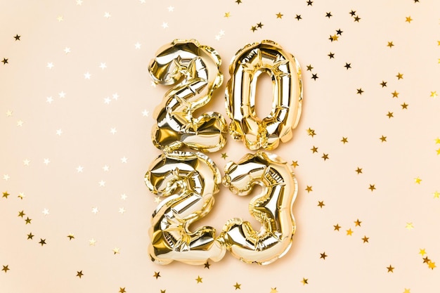 New year 2023 balloon celebration card gold foil helium balloon
number 2023 party decoration gold confetti stars on beige
background flat lay merry christmas happy holidays concept