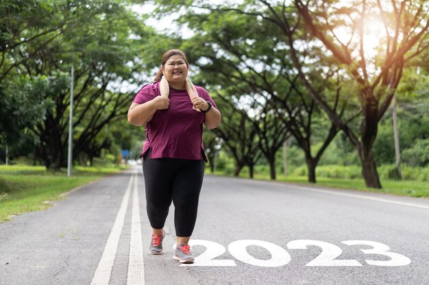 2023年新年またはスタートストレートコンセプトワード2023がアスファルト道路に書かれ、アジアの太った女性が減量を実行する準備ができています