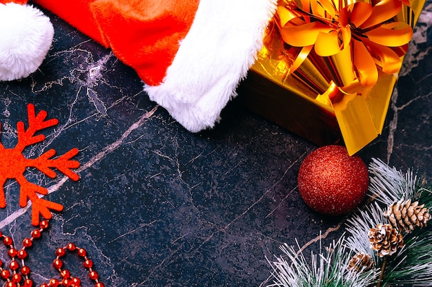 Фото Новогодние и рождественские подарки. выборочный фокус. шапка деда мороза, коробки с подарками, бусы, елочные игрушки на темном фоне.