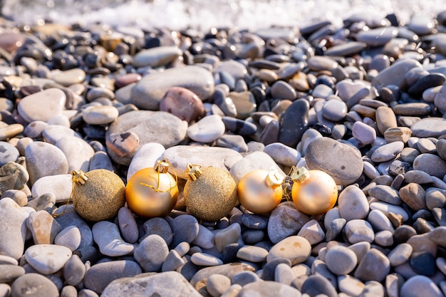 Photo new year at the beach christmas ornaments standing on stones near the waterchristmas holiday decorat...