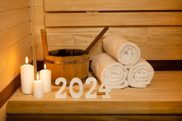 New Year card Sauna numbers 2024 wooden white towel bucket and candles holiday poster copy space