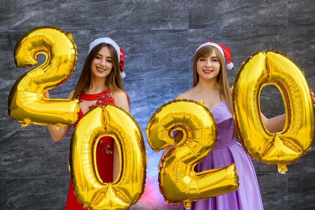 Photo new year celebration concept. two beautiful women with golden air balloons 2020