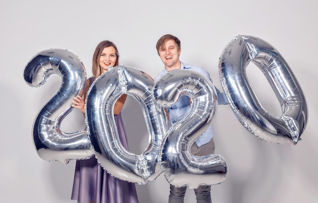 New year, celebration and holidays concept - love couple having fun with sign 2020 made of silver balloons for new year