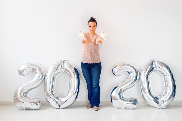 New Year celebration and party concept - Happy young woman with sparklers near silver 2020 balloons.