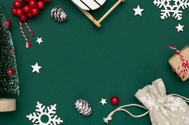 New year and christmas composition from white snowflakes, decorative chrismas tree and sledge, cones and red berries on green paper background. top view, copy space, flat lay.