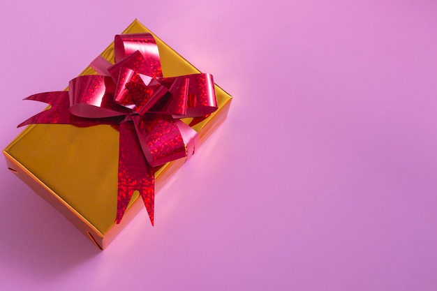 New Year Christmas composition. Gold gift with a red bow on a pink background. Top View Copy Space New Year 2022 Christmas