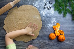 New year and christmas decorations on a wooden surface with tangerines and a christmas tree the hands of a small child make molds for cooking gingerbread in the form of a man