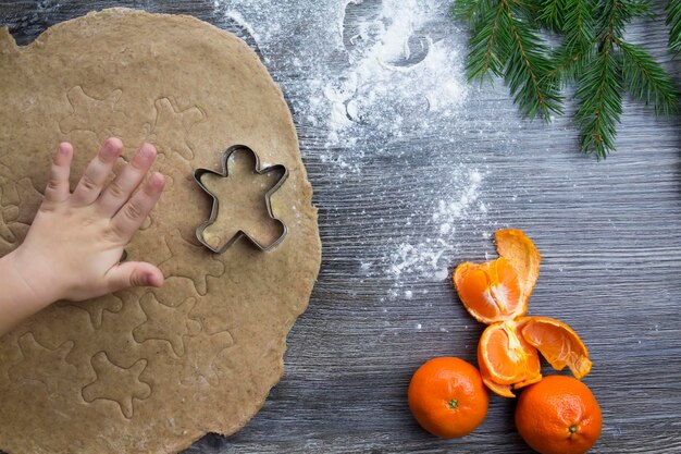 New Year and Christmas decorations on a wooden surface with tangerines and a Christmas tree The hands of a small child make molds for cooking gingerbread in the form of a man