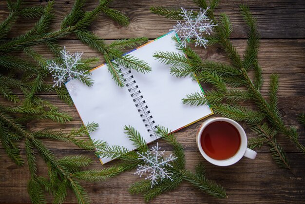 New year and Christmas festive picture with fir branches, snowflakes, tea, open notepad on a wooden rustic background