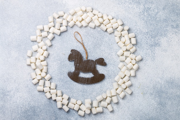 New Year or Christmas flat lay top view with marshmallows and rustic wooden horse toy 