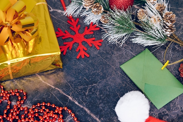 Новогодние и рождественские подарки. Выборочный фокус. Шапка Деда Мороза, коробки с подарками, бусы, елочные игрушки на темном фоне.