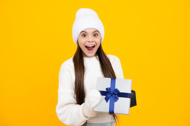 New year or christmas holiday gift portrait of a teenager child\
girl holding present box isolated over yellow studio background\
present greeting and gifting concept birthday holiday concept
