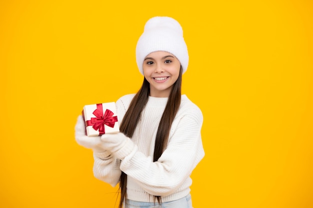 New year or christmas holiday gift portrait of a teenager child
girl holding present box isolated over yellow studio background
present greeting and gifting concept birthday holiday concept