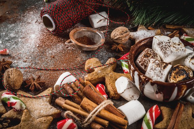 New Year, Christmas treats, sweets. Cup of hot chocolate with fried marshmallow, ginger star cookies, gingerbread men, striped candy, spices cinnamon anise, cocoa, powdered sugar.  