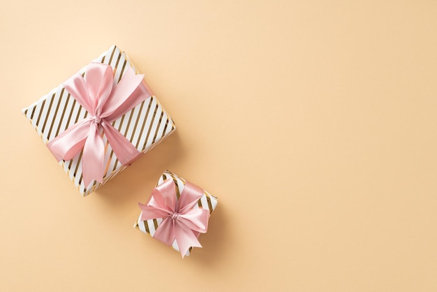 Новогодняя концепция Фотография стильных подарочных коробок с розовыми ленточными бантами, вид сверху на изолированном светло-бежевом фоне с копировальным пространством