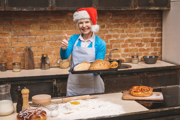 Cucina di capodanno. il ritratto della donna invecchiata senior attraente sta cucinando sulla cucina. nonna che produce cottura saporita di natale.