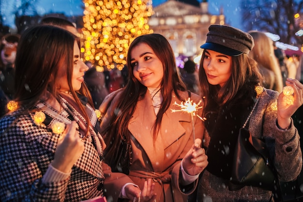 Vigilia di capodanno donne amiche che bruciano le stelle filanti a lviv vicino all'albero di natale sulla fiera di strada che celebra