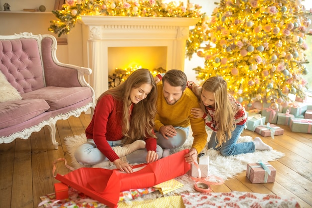 Regali di capodanno. giovane famiglia seduta sul pavimento e confezionamento di regali di capodanno