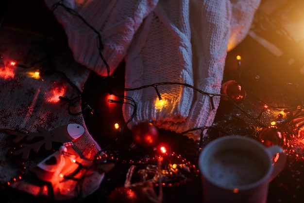 New Year, holiday, celebration, winter concepts. Beige warm knitted sweater, garland and red Christmas toys on a black background in the dark