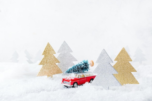 写真 年末年始のコンセプト雪の森でクリスマスツリーを運ぶ赤いおもちゃの車お祭りの装飾が施されたコピースペースグリーティングカード