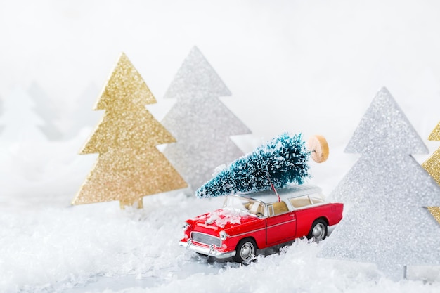 New year holiday concept Red toy car carrying christmas tree in a snow forest Copy space greeting card with festive decoration