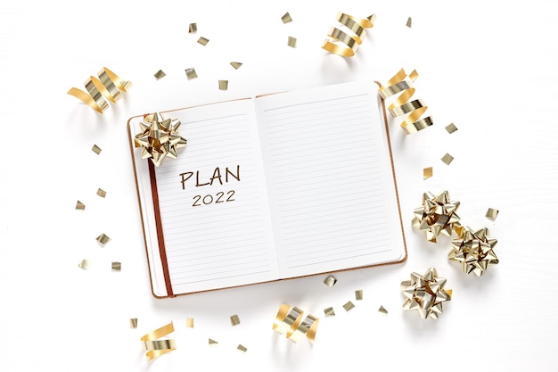 New Year. Holiday decorations and notebook with wish list on white table, flat lay style. Planning concept.