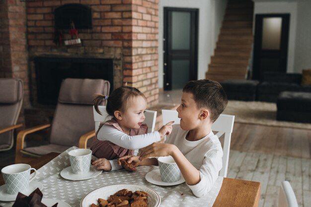 New year at home. A girl in a pink dress with ponytails. In anticipation of the holiday. Two children. Sister feeds brother. Drink tea in the kitchen with gingerbread.