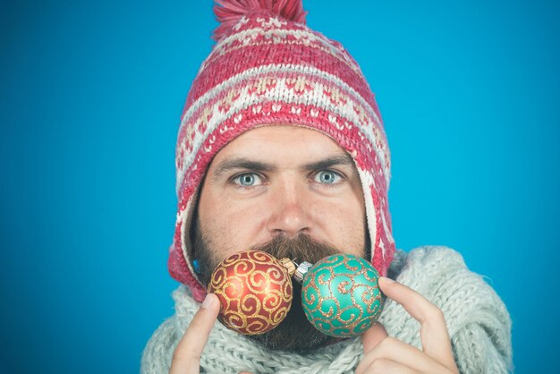 New year man with serious face with long beard in winter hat and scarf holds new years toys for fir