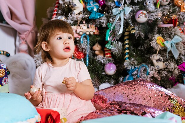 New year merry christmas happy holidays portrait of little girl in pink dress sits on floor with pil...