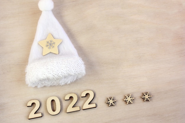 New year number 2022 lined with wooden figures on the wooden
surface next to the white christmas hat.