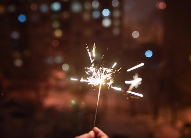 New year party burning sparkler closeup in female hand on black background Christmas light