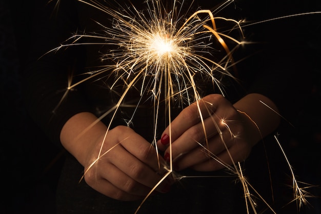 Foto primo piano della scintilla ardente della festa di capodanno in mani femminili sul nero.